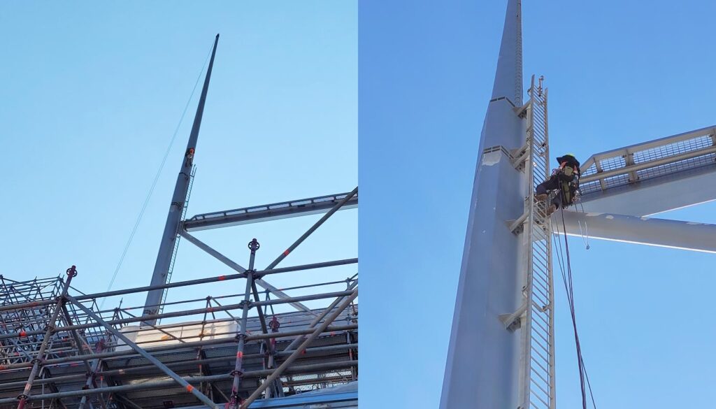 A worker is rappelling down the blade of a wind turbine for maintenance, with scaffolding visible nearby.