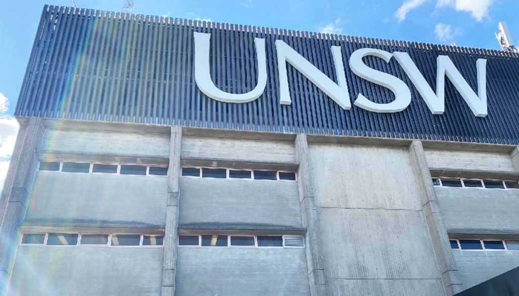 A low-angle view of the UNSW building with large white lettering against a dark facade and a blue sky.