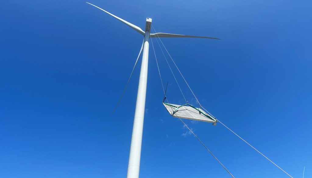 A low-angle view of a wind turbine with a suspended platform attached for maintenance.
