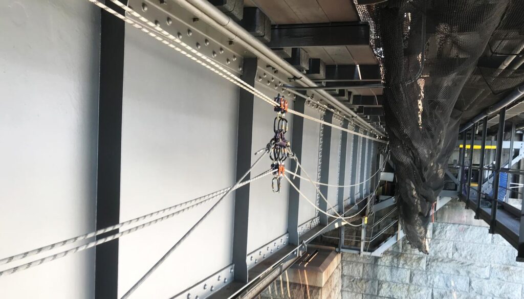 A close-up view of a zip line course with cables, pulleys, and safety equipment attached to a building structure.