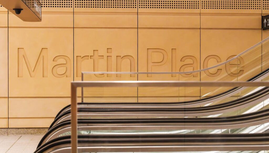 The words Martin Place are carved into a golden wall above an escalator in a subway or train station.