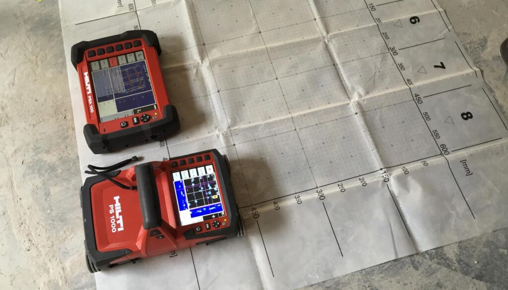 Two red Hilti PS1000 concrete scanners are positioned on a gridded mat, likely for non-destructive testing.