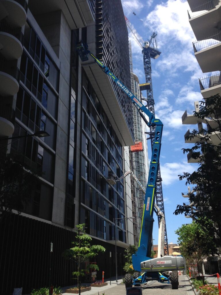 A boom lift is positioned against the side of a high-rise building under construction on a sunny day.