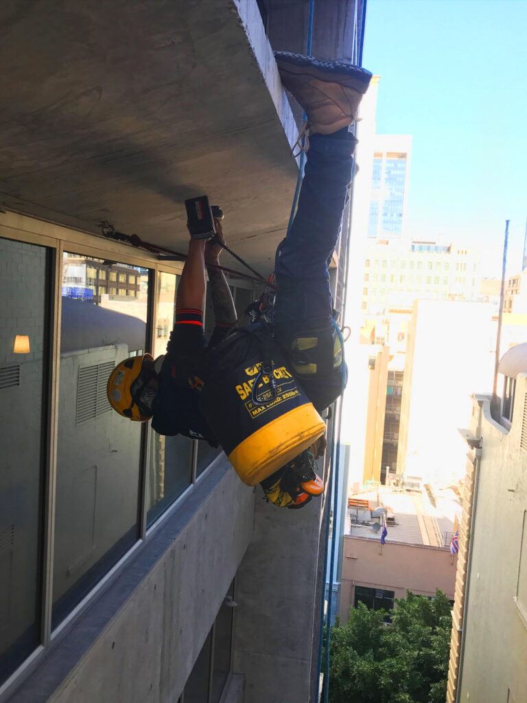 A window washer hangs suspended from a high-rise building, cleaning a window.