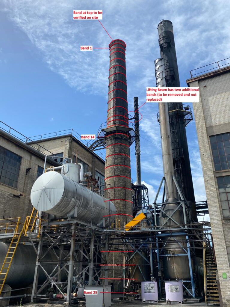 Industrial facility with two tall smokestacks, one marked with red lines indicating numbered bands for inspection/maintenance.
