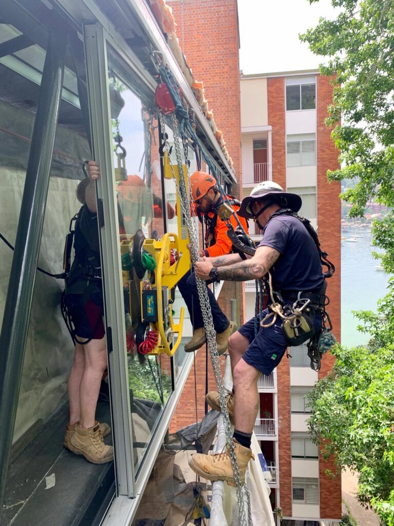 Window washers are suspended from a platform while cleaning the glass facade of a tall building.