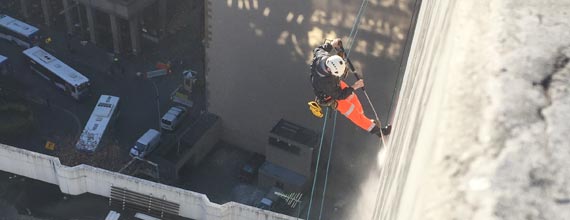 A person in climbing gear rappels down the side of a tall building.