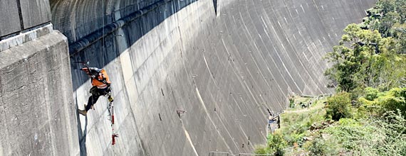 A worker rappels down the face of a large concrete dam.