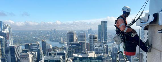 A window washer is suspended on ropes while cleaning a high-rise building with a cityscape view.
