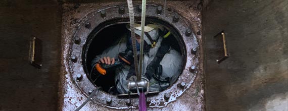 A worker in protective gear is partially visible inside a circular opening in a metal structure.